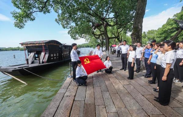 Members of the Communist Party of China (CPC) review the Party admission oath beside the replica of a boat, now referred to as the Red Boat, on which CPC founders concluded their meeting in 1921, on Nanhu Lake in Jiaxing, East China's Zhejiang province, June 30, 2025. (Photo/Xinhua)