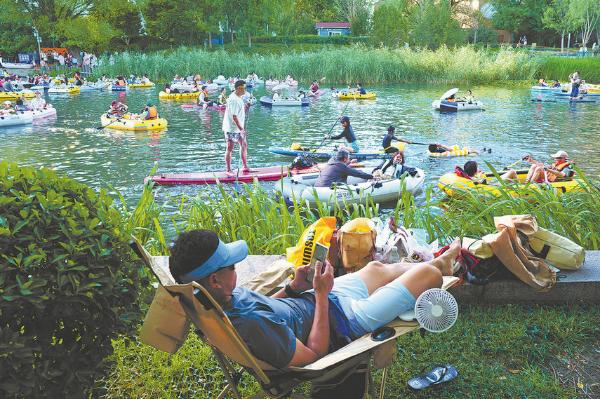 People relax on the banks of the Liangma River, while others go paddling and kayaking on the water, on June 20 in Beijing. (Photo by Wei Xiaohao/China Daily)